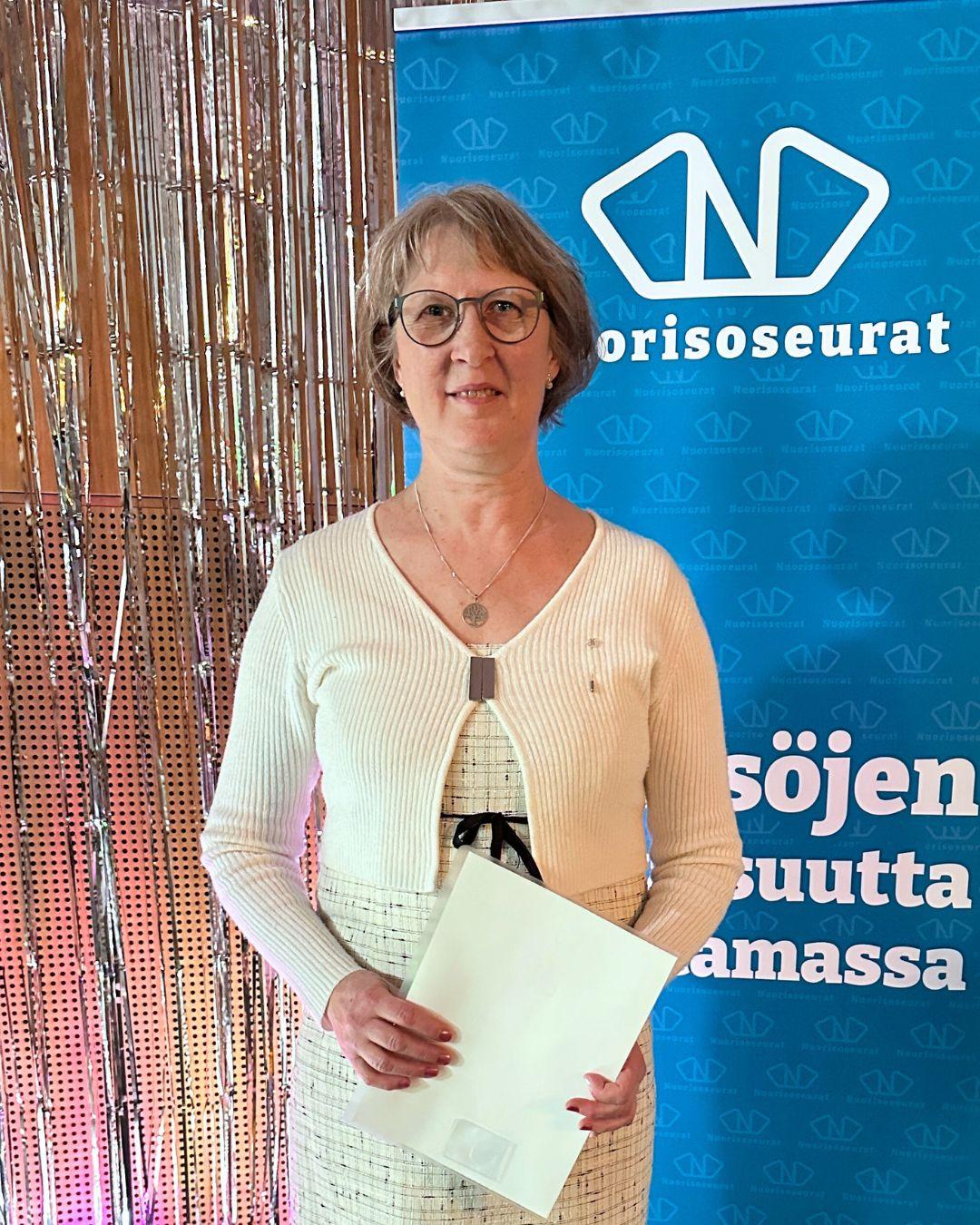 Tuula Honkala seisomassa Nuorisoseurojen roll up:in edessä.